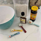 Baking ingredients and utensils on a countertop including a mixing bowl, measuring spoons, and bottles.