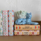 Decorative blue cat figurine on a stack of books with a white wall background