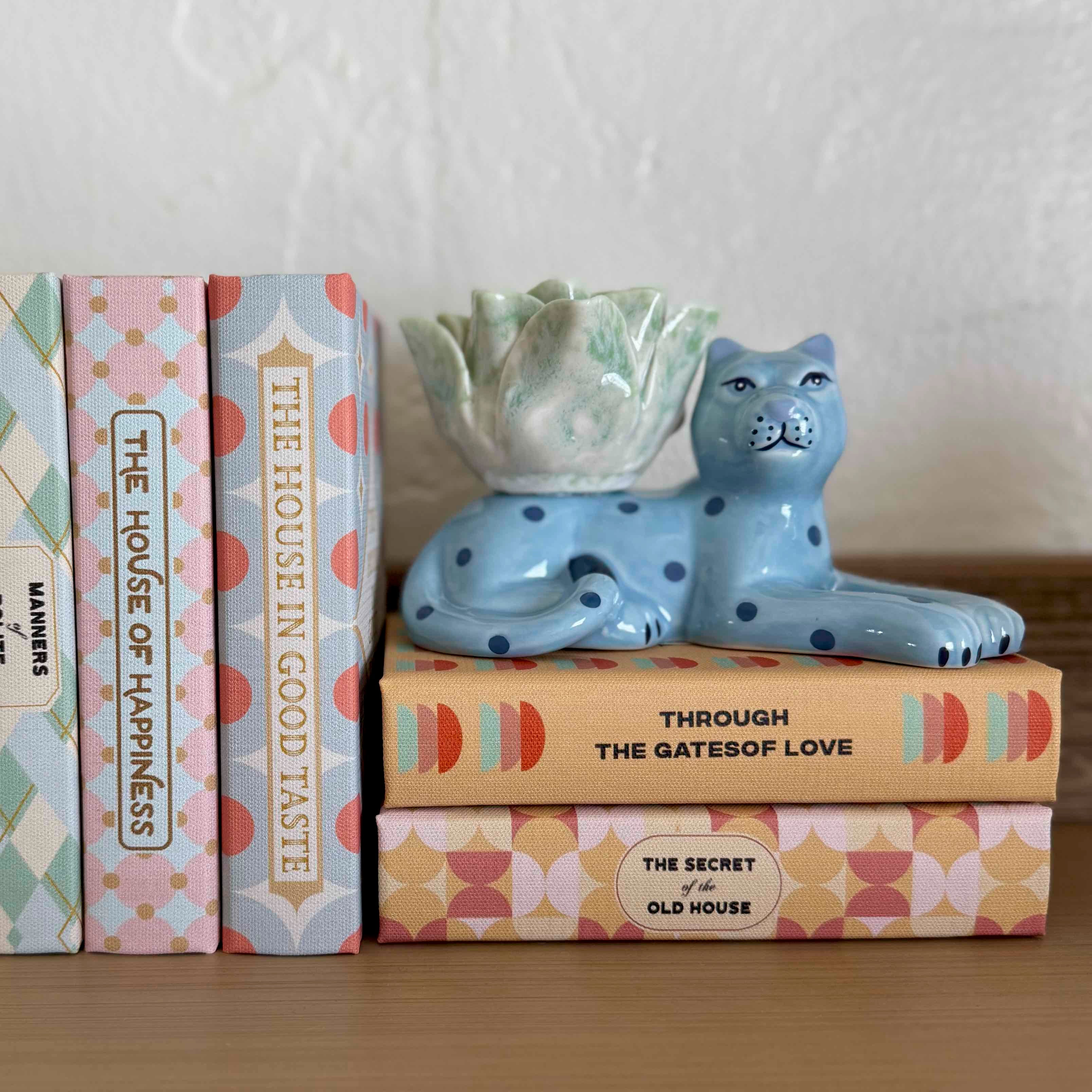 Decorative blue cat figurine on a stack of books with a white wall background
