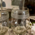 Two clear glass tumblers with leaf patterns on a reflective surface.