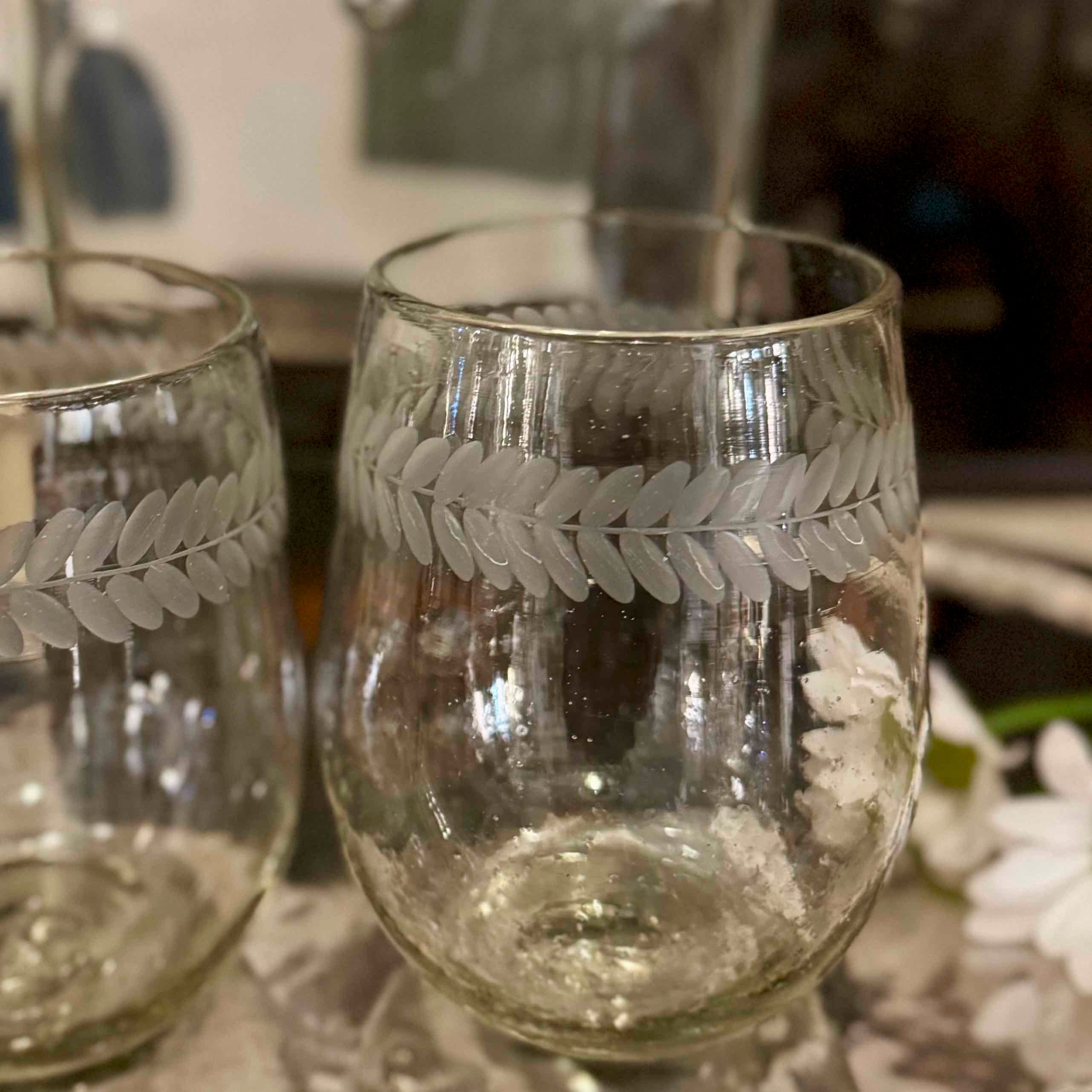 Two clear glass tumblers with leaf patterns on a reflective surface.