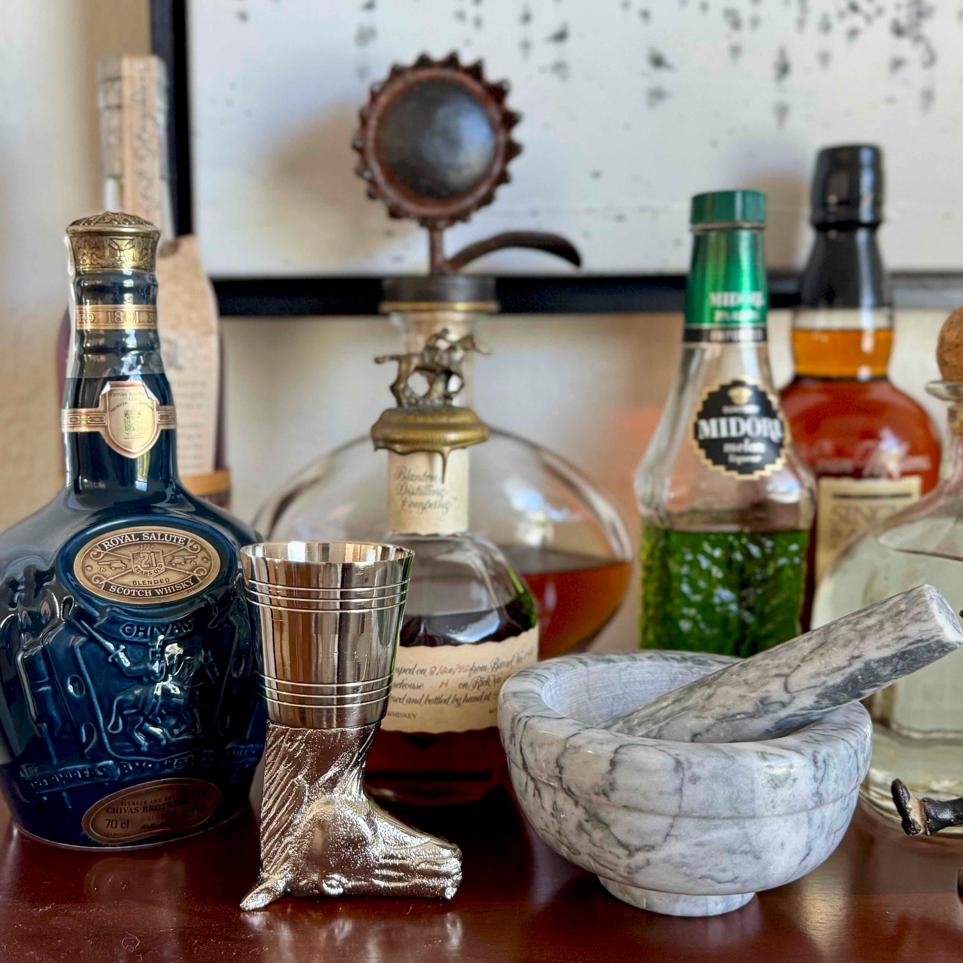 Alcohol bottles including Johnnie Walker Blue Label and Midori with a mortar and pestle on a wooden surface.