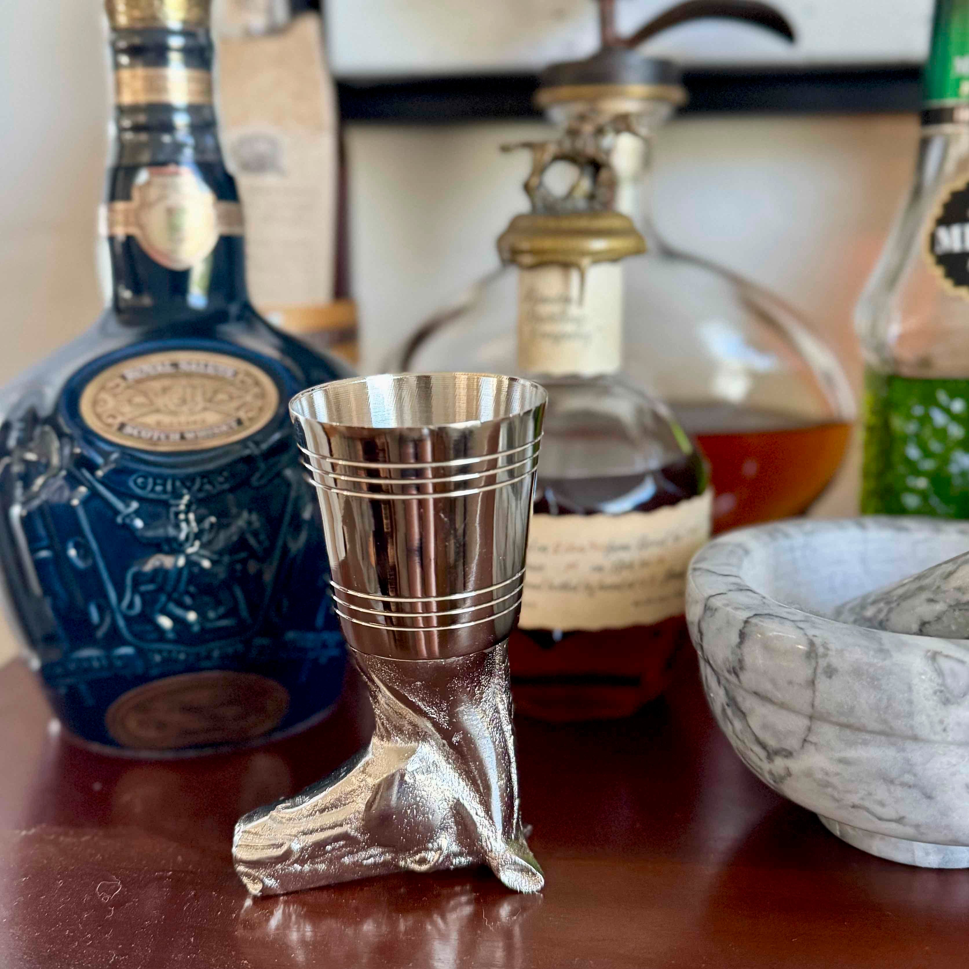 Metallic boot-shaped shot glass on a bar with bottles in the background