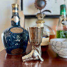 Silver boot-shaped shot glass in front of a bottle of Johnnie Walker Blue Label whisky.