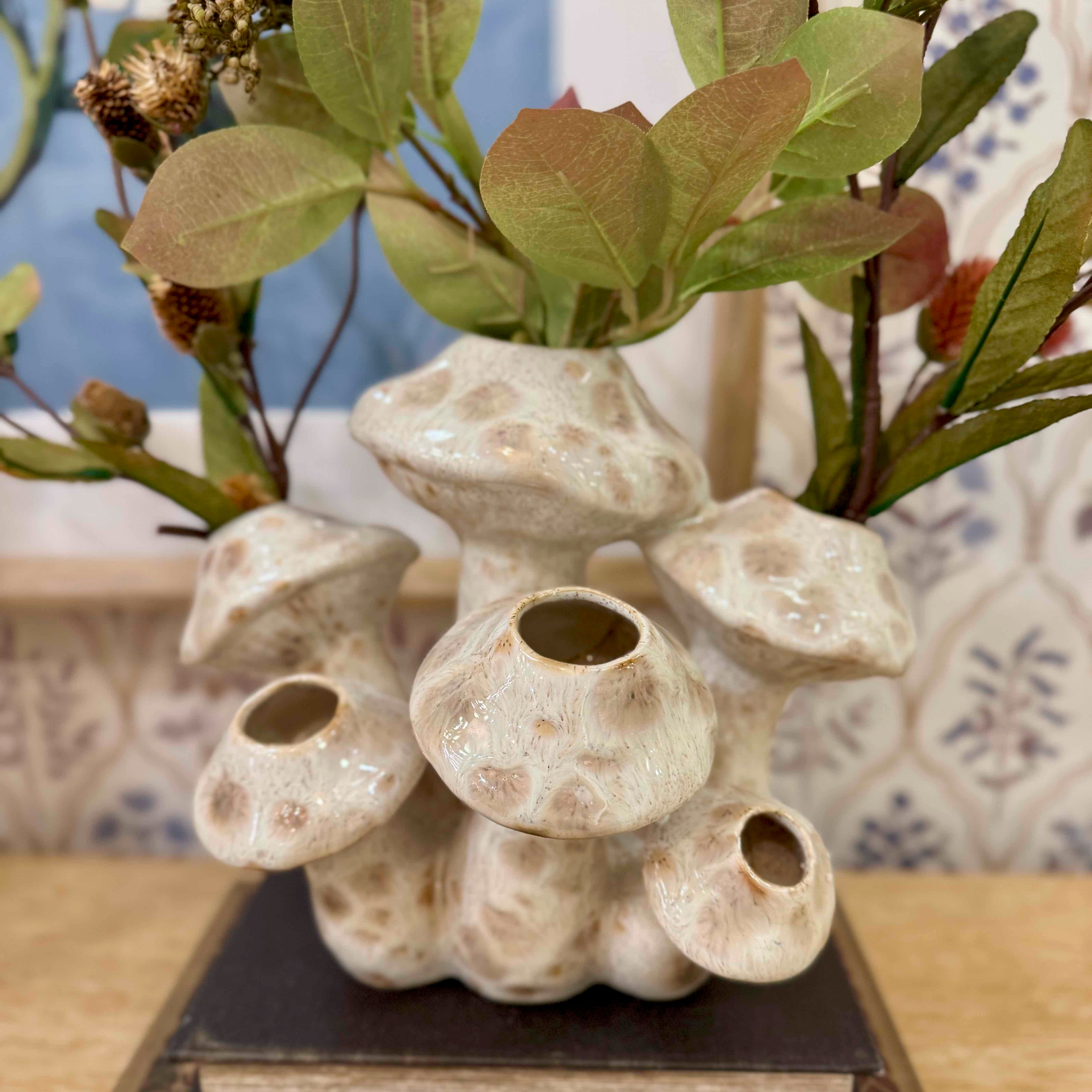 Ceramic vase with multiple nozzles holding green leaves on a wooden surface.