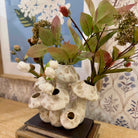 Decorative vase with artificial plants on a table against a floral wallpaper background