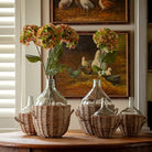 Decorative setup with clear glass bottles, wicker baskets, and flowers on a wooden table.