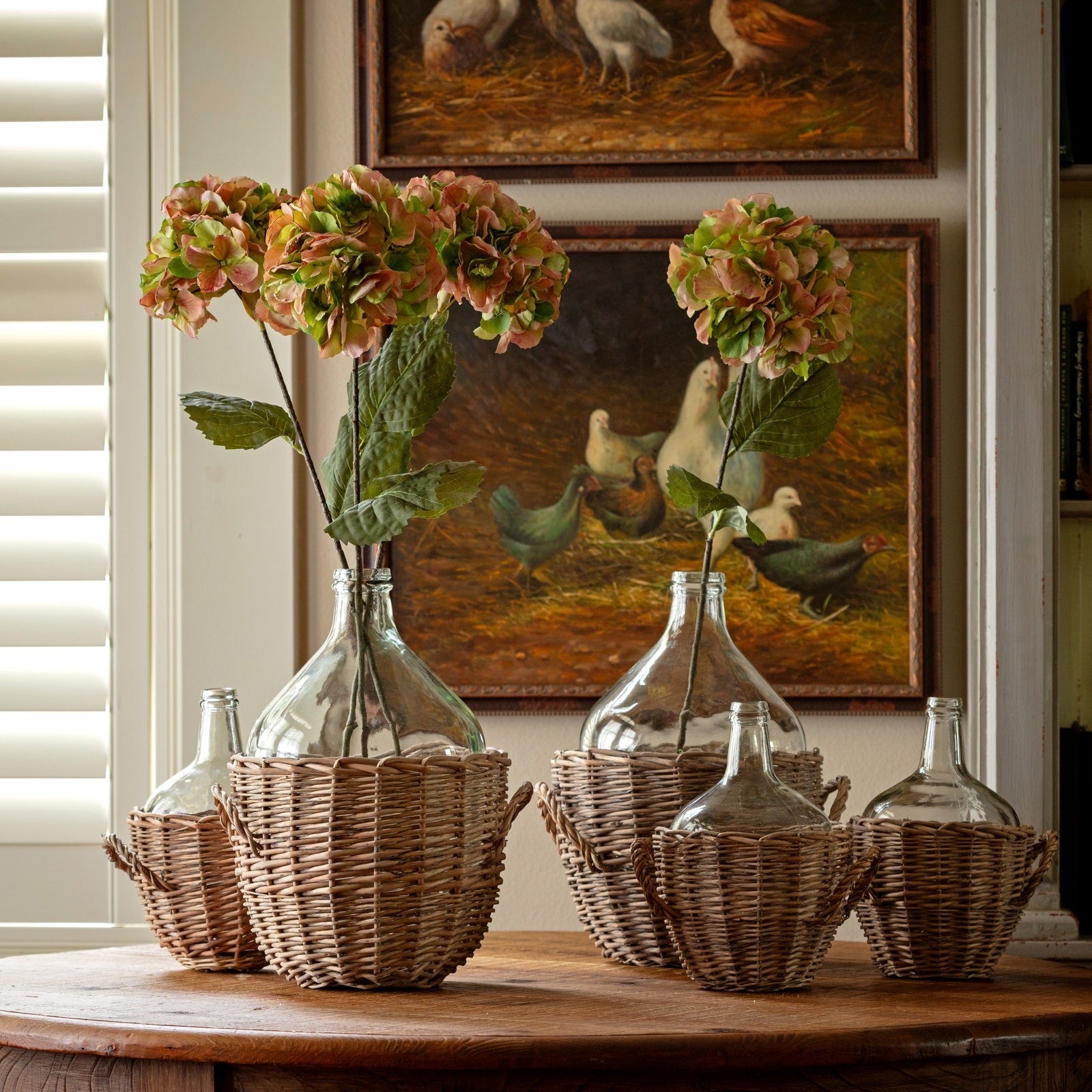 Decorative setup with clear glass bottles, wicker baskets, and flowers on a wooden table.