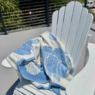 Blue and white floral-patterned towel draped over a white Adirondack chair outdoors.