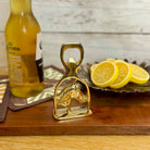 Gold horse-shaped bottle opener on a wooden surface with a Corona Extra bottle and lemon slices in the background.
