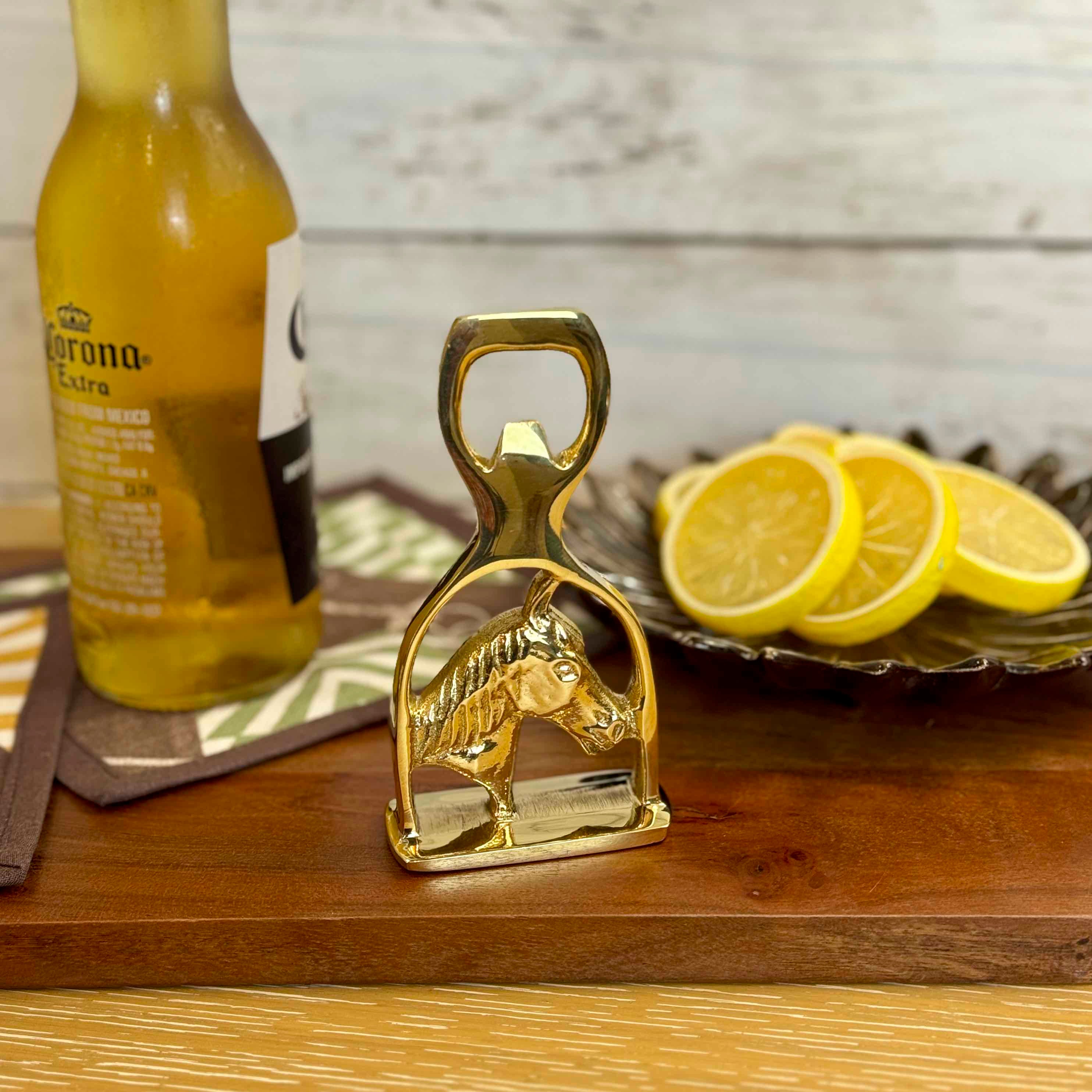 Gold horse-shaped bottle opener on a wooden surface with a Corona Extra bottle and lemon slices in the background.