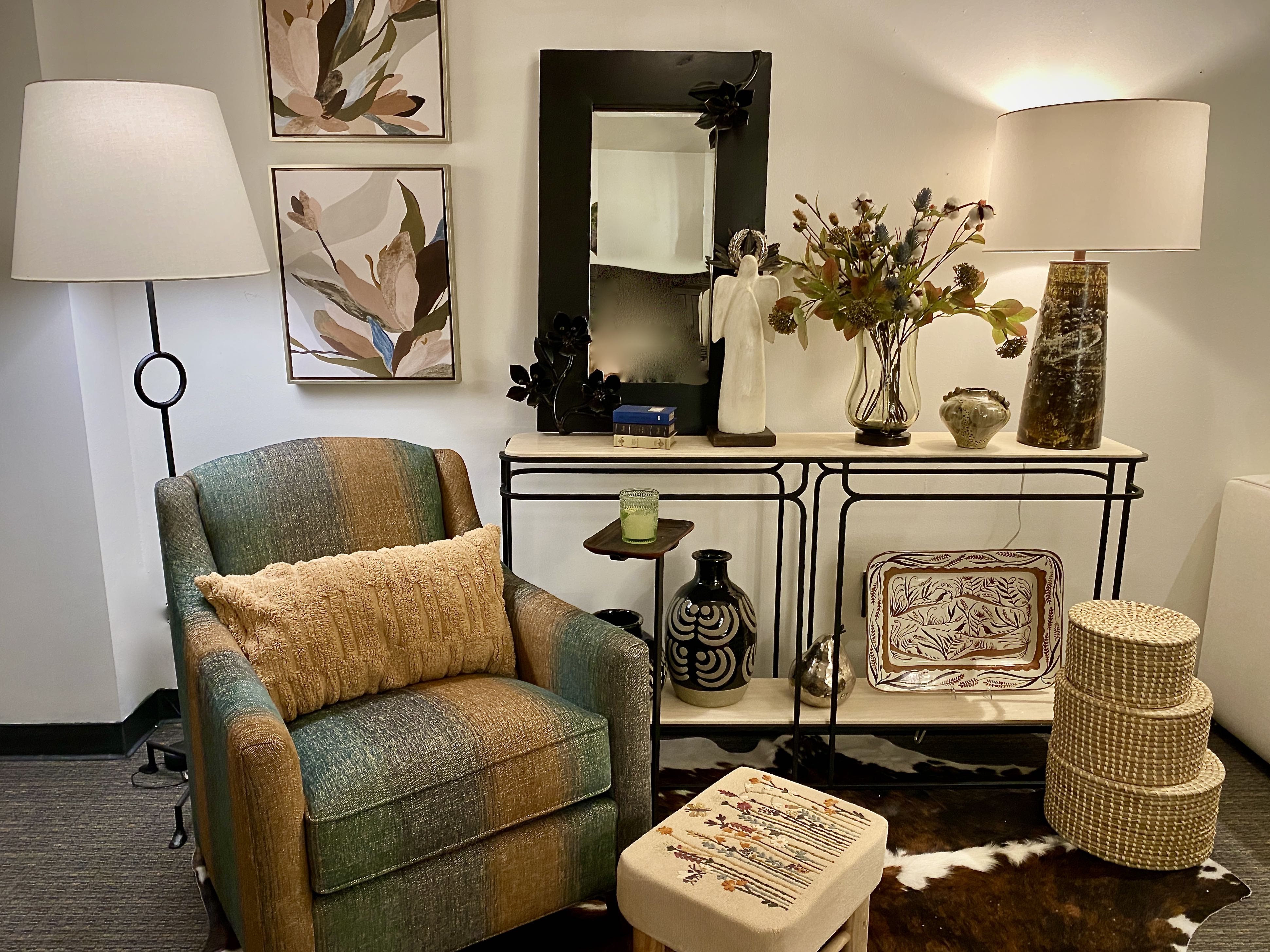 Ranch Style casual home decor including a cowhide rug, embroidered foot stool, plaid arm chair, ceramic table lamp, Wood and iron mirror, concrete angel, stoneware and baskets.