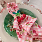 Decorative table setting with pink checkered napkin and cherry design on a green plate.