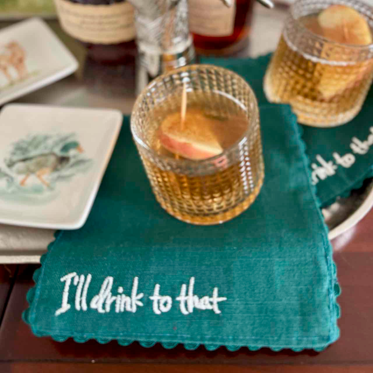 Teal napkin with 'I'll drink to that' text on a table with drinks and plates.