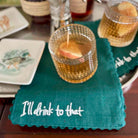 Teal napkin with 'I'll drink to that' text on a table with drinks and plates.