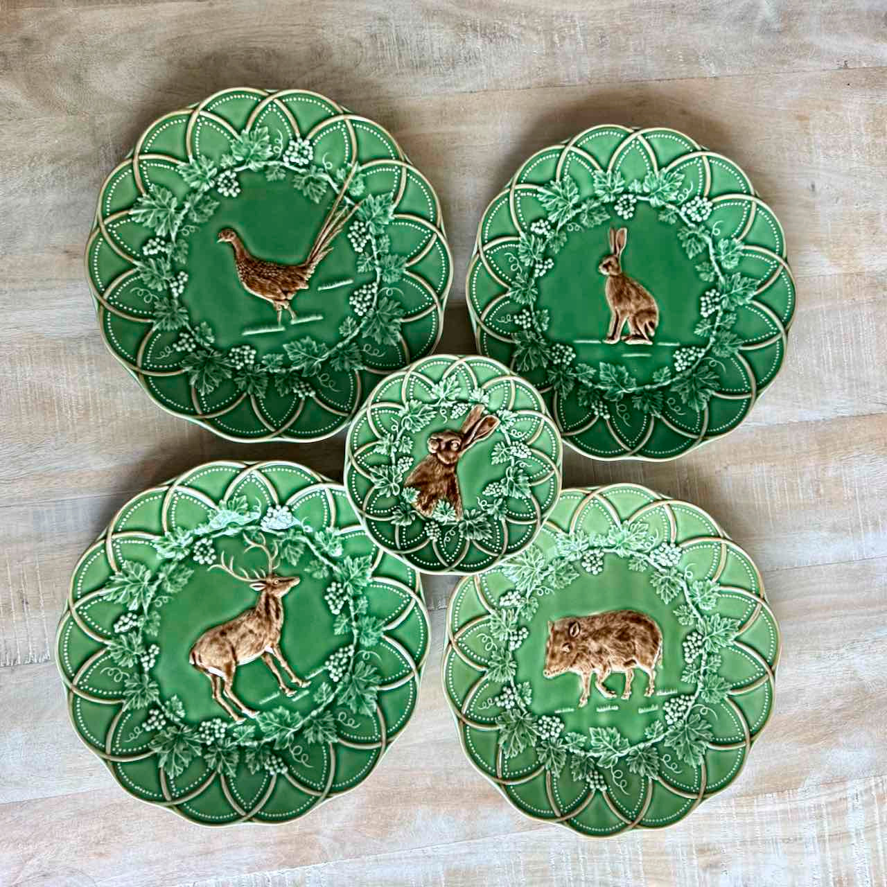 Set of five green ceramic plates with animal illustrations on a wooden surface