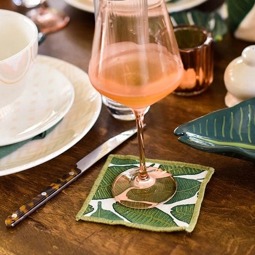 Glass of pink wine on a leaf-patterned coaster with a wooden table setting.