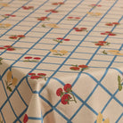 A close-up of a tablecloth with a cream background, a blue grid pattern, and small red and yellow floral motifs.