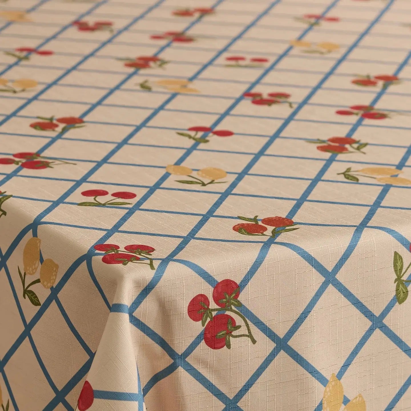 A close-up of a tablecloth with a cream background, a blue grid pattern, and small red and yellow floral motifs.