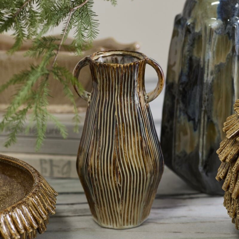 Decorative ceramic vase with textured design on a wooden surface with plants and other decorative items.