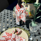 Wine bottle with decorative napkin on a table with a glass and other items.