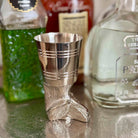 Silver boot-shaped jigger with bottles of tequila in the background