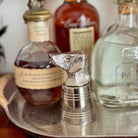 Silver jigger on a tray with liquor bottles in the background