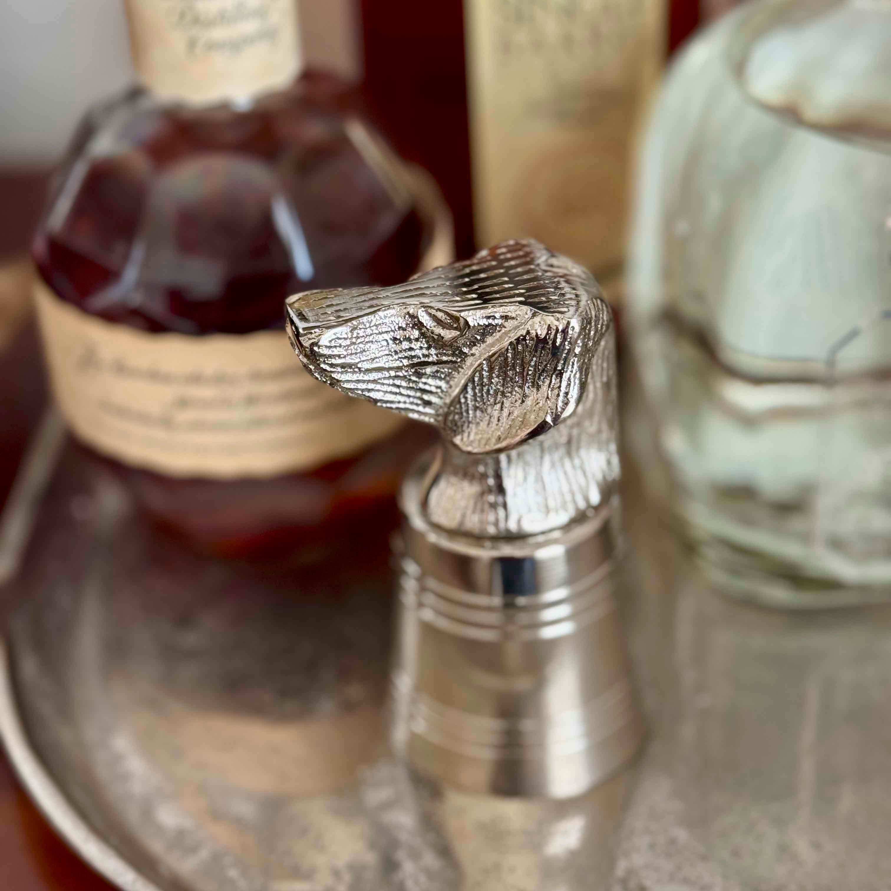 Close-up of a silver horse head bottle stopper with bottles in the background.