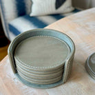 Set of round gray coasters in a holder on a wooden surface.