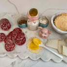Platter with sliced salami, crackers, and a small container of yellow spread on a marble surface.