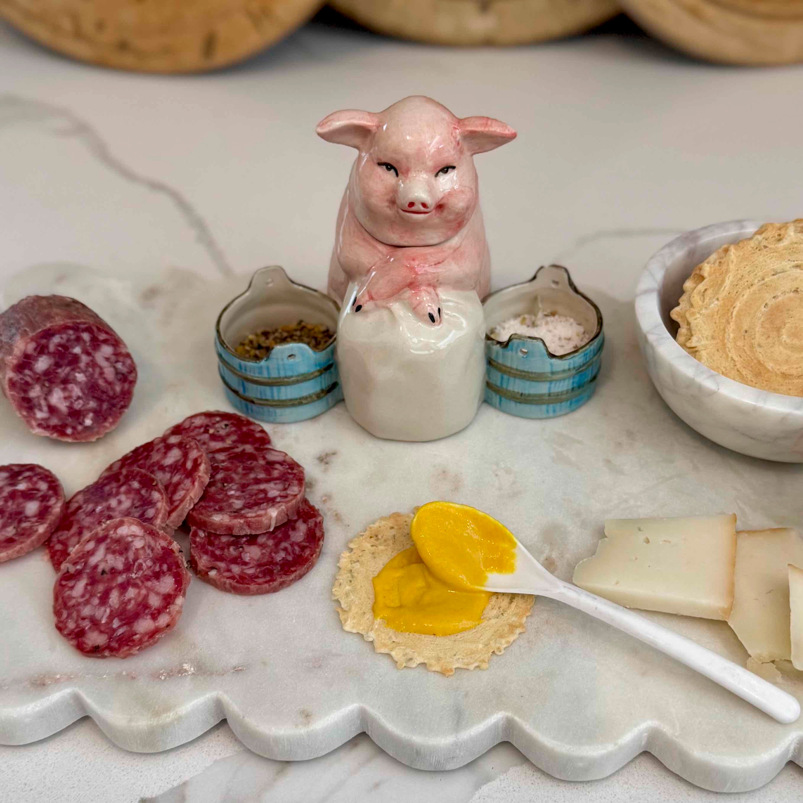 Marble surface with cured meats, crackers, cheese, and a pig-shaped salt shaker.
