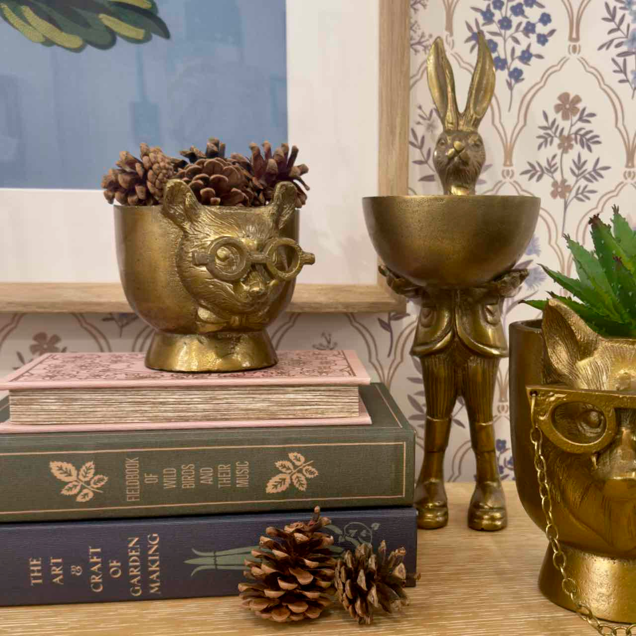 Decorative brass animal figurines on books with a floral wallpaper background