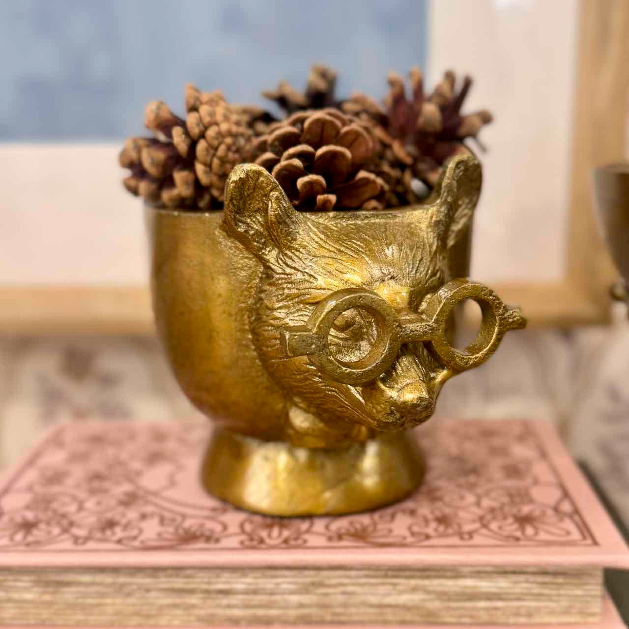 Gold owl-shaped container with pinecones on a decorative surface