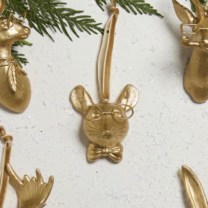 Gold mouse ornament with glasses and bow tie on a textured white surface with greenery.