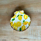 A scalloped ceramic dish featuring a yellow lemon print on a white background, set on a light wood surface.