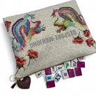 A decorative zippered pouch with a beige patterned background, embroidered phoenix motifs in blue, pink, and green, and red rose illustrations. The pouch is shown open with several miniature mahjong tiles arranged in front, and a dark purple heart-shaped tassel keychain hangs from the zipper.