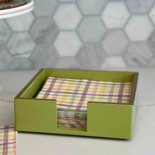 Green napkin holder with plaid napkins on a tiled bathroom counter.