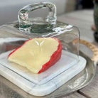 Glass-covered cheese platter with a wedge of cheese on a marble base.