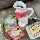 Decorative pitcher with a pink interior on a table with glasses and a dish.