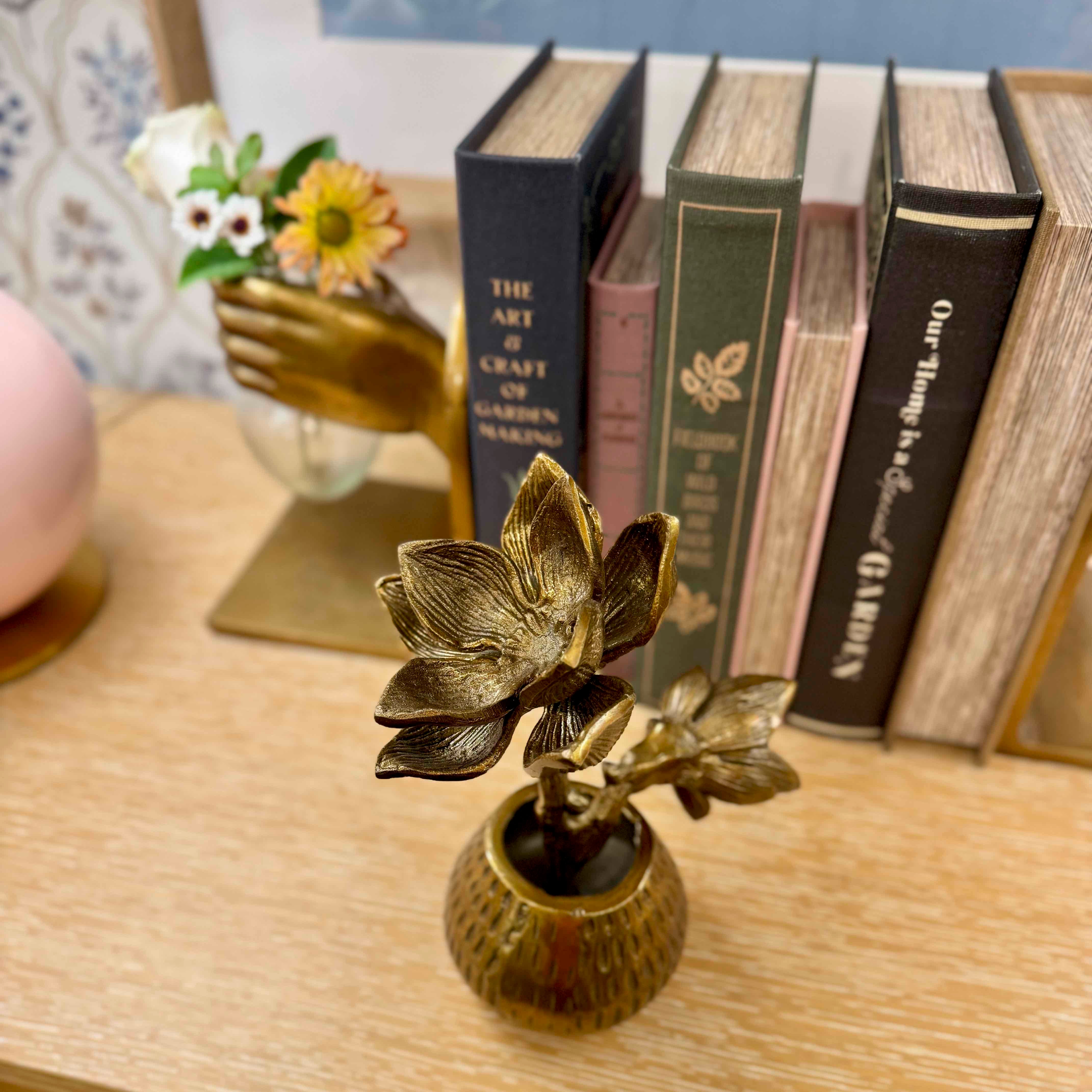 Bronze lotus flower sculpture on a wooden surface with books in the background