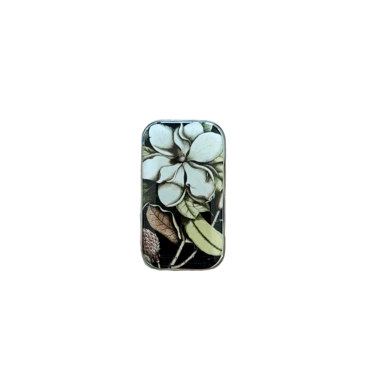 A rectangular metal tin with a vintage-style floral illustration featuring white flowers and green leaves on a dark background, placed on a light wood surface.