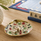 A decorative ceramic dish shaped like a shell, featuring a white and gold Mahjong tile pattern, holding three white dice with black markings on a wooden tabletop.