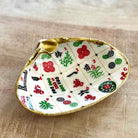 A decorative shell-shaped dish featuring a printed Mahjong tile pattern with gold trim, photographed on a light wood surface.