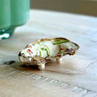 A small decorative shell-shaped object with three white feet, featuring a white interior printed with green and red abstract patterns, resting on a light wooden surface.
