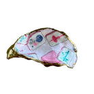 A handmade gold-rimmed shell-shaped dish or tray decorated with colorful printed tile patterns on a light wood background.