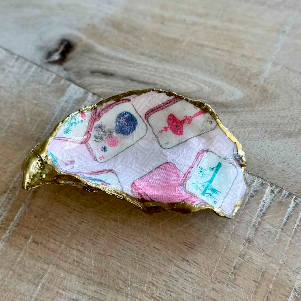 A handmade gold-rimmed shell-shaped dish or tray decorated with colorful printed tile patterns on a light wood background.