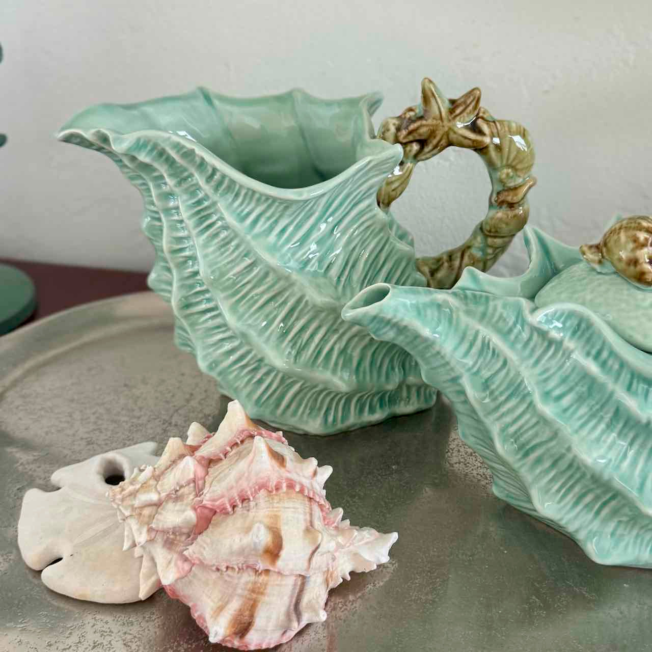 Two green ceramic shell-shaped vases with a seashell on a gray surface.