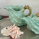 Two green ceramic shell-shaped vases with a seashell on a gray surface.