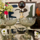 Two glass dessert bowls on a reflective surface with a decorative background