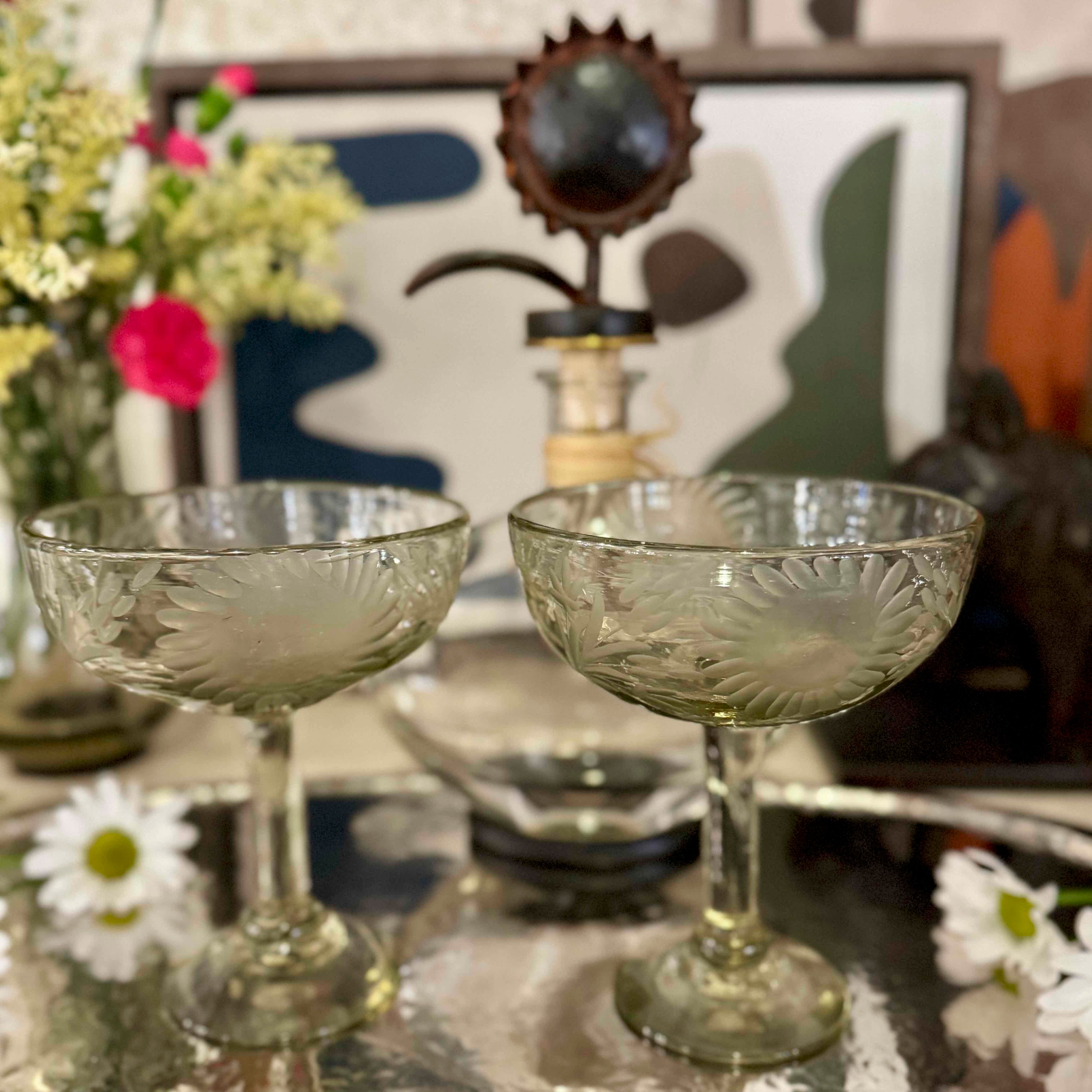 Two glass dessert bowls on a reflective surface with a decorative background